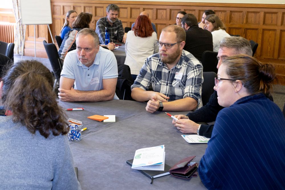 Five attendees, three male and two female) at a conference sitting at a round black clothed table